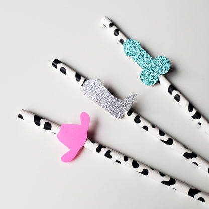 cowprint straws are adorned with glitter penis shapes, bright pink cowgirl hats, and silver glitter boots perfect for bachelorette party decorations with a nashville theme
